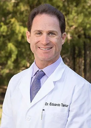 Portrait image of Eduardo Tanur, D.D.S., M.S. standing in a white coat outside.