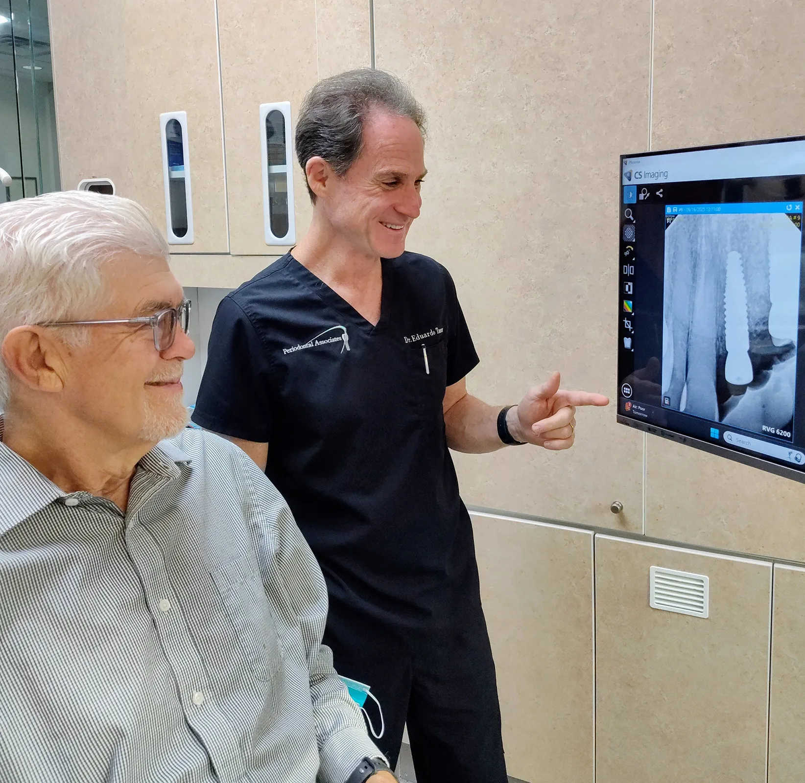 Dr. Tanur and a patient observing a dental implant X-ray on a screen